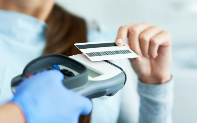 Person in blue gloves holding credit card over payment terminal for transaction.
