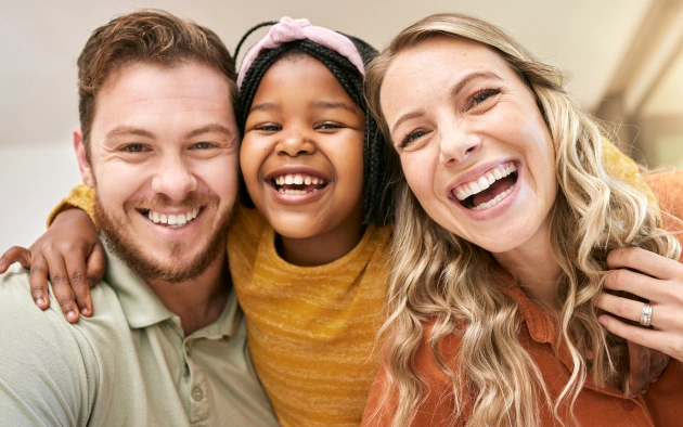 Three smiling friends posing together indoors, displaying healthy, bright smiles.