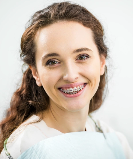 Young girl smiling at camera wearing braces in professional orthodontic portrait setting.