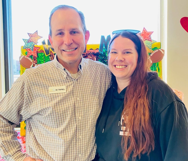 Two smiling professionals posing together in an orthodontic office with colorful artwork background.