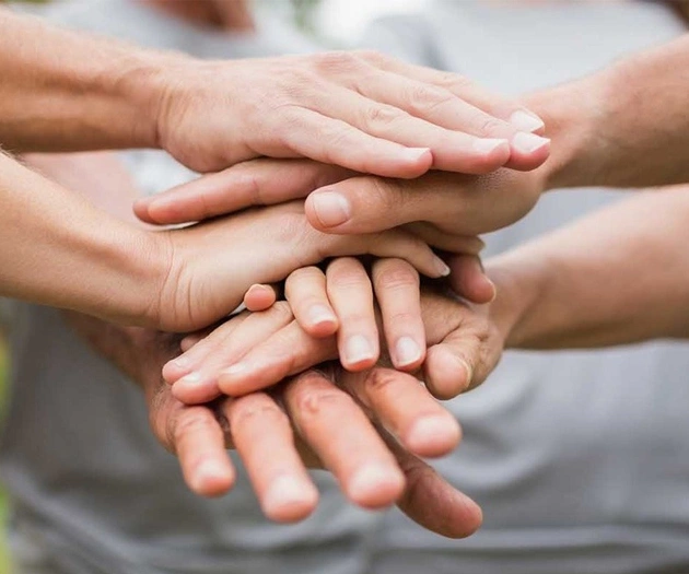 Multiple hands stacked together showing unity, teamwork, and community support in orthodontics practice.