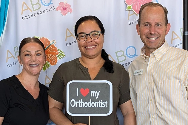 Three people posing at ABQ Orthodontics event, middle person holding "I love my Orthodontist" sign.