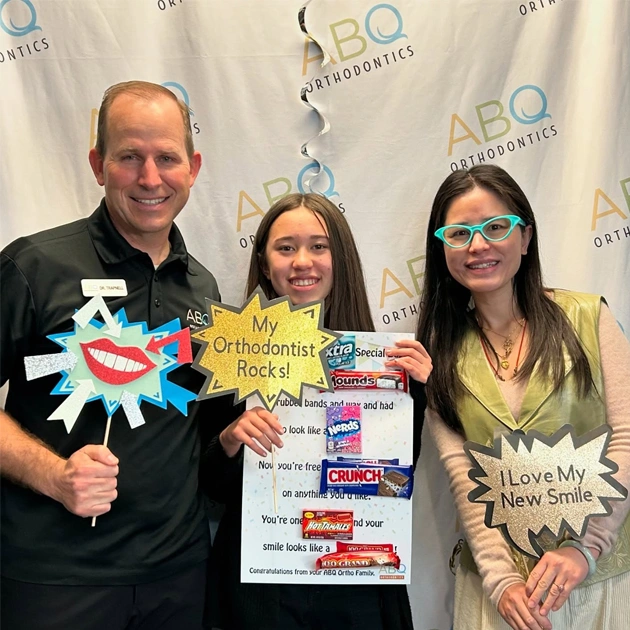 Three people holding orthodontic awards at ABQ Orthodontics event with branded backdrop.