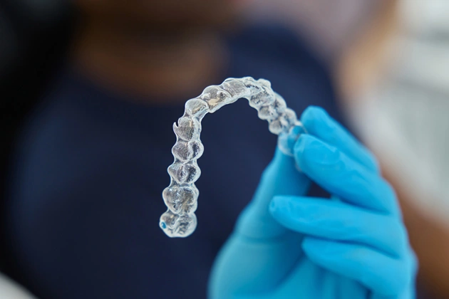 Orthodontist in blue gloves holding clear aligner tray for dental treatment.