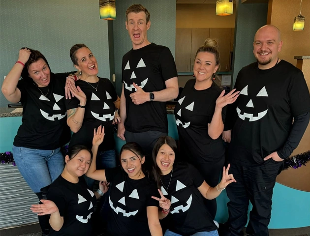 Team members wearing matching black Halloween ghost shirts posing together indoors at ABQ Orthodontics office.