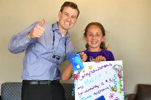 Man and girl holding colorful poster, giving thumbs up in office setting.