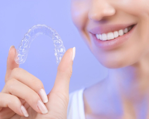 Smiling woman holding clear invisible aligner against purple background