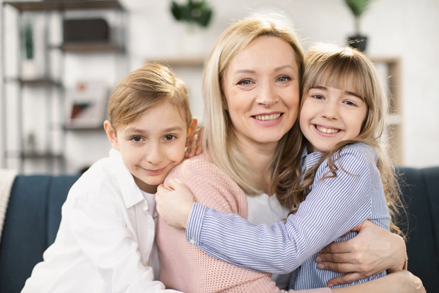 Mother with two smiling children hugging in bright, modern home interior