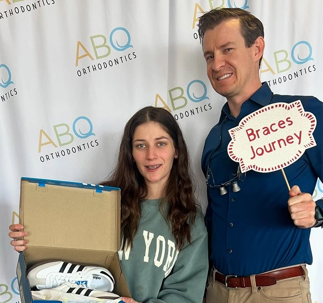 Two people at ABQ Orthodontics event holding braces-themed sign and gift box