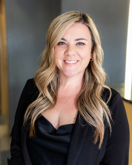 Professional woman with blonde wavy hair smiling at camera in office setting for ABQ Orthodontics.