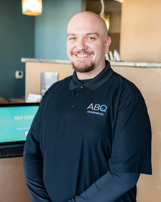 Male staff member wearing ABQ Orthodontics polo shirt smiling in modern office setting.