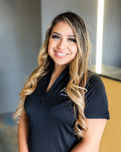Professional woman smiling at camera in black polo shirt, indoor clinical setting.