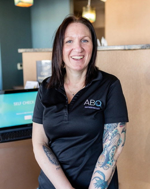 Woman wearing ABQ Orthodontics polo shirt smiling in modern dental office reception area.