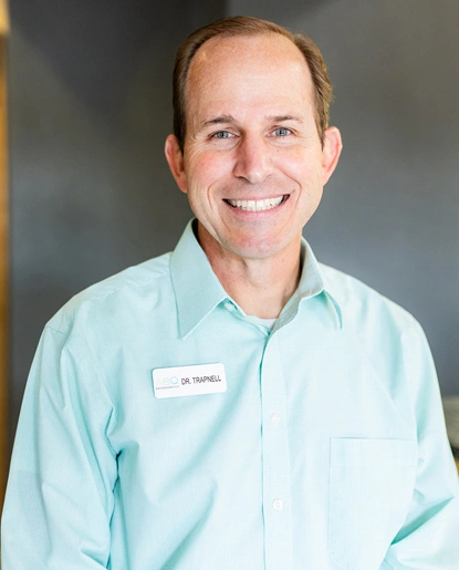 Professional headshot of male orthodontist in light blue shirt against neutral background.