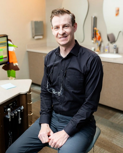 Male orthodontist smiling at camera in modern dental office treatment room.
