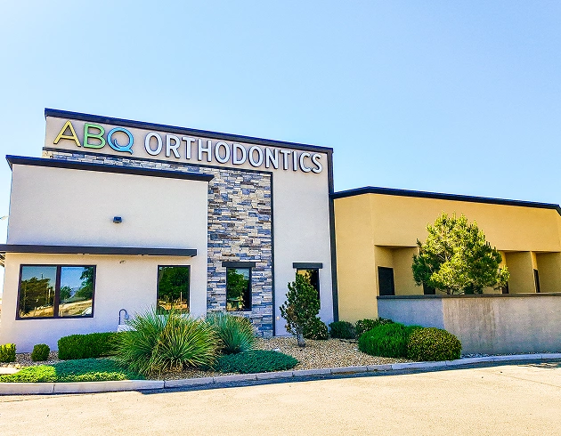 ABQ Orthodontics modern dental office building with stone and yellow exterior under clear sky.