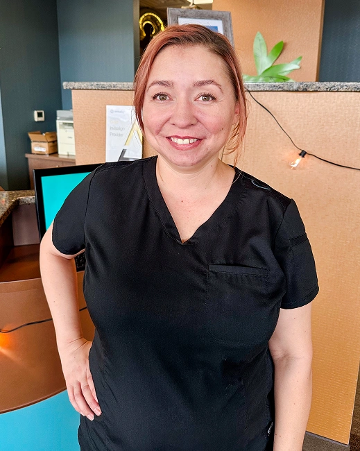 Woman in black scrubs smiling at camera in modern orthodontic office setting.