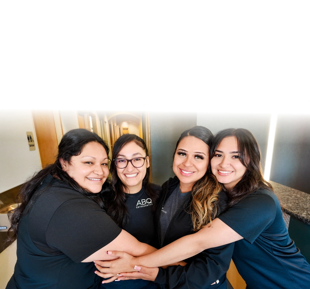 Four women smiling with hands together in orthodontic office setting, showing team unity and camaraderie.