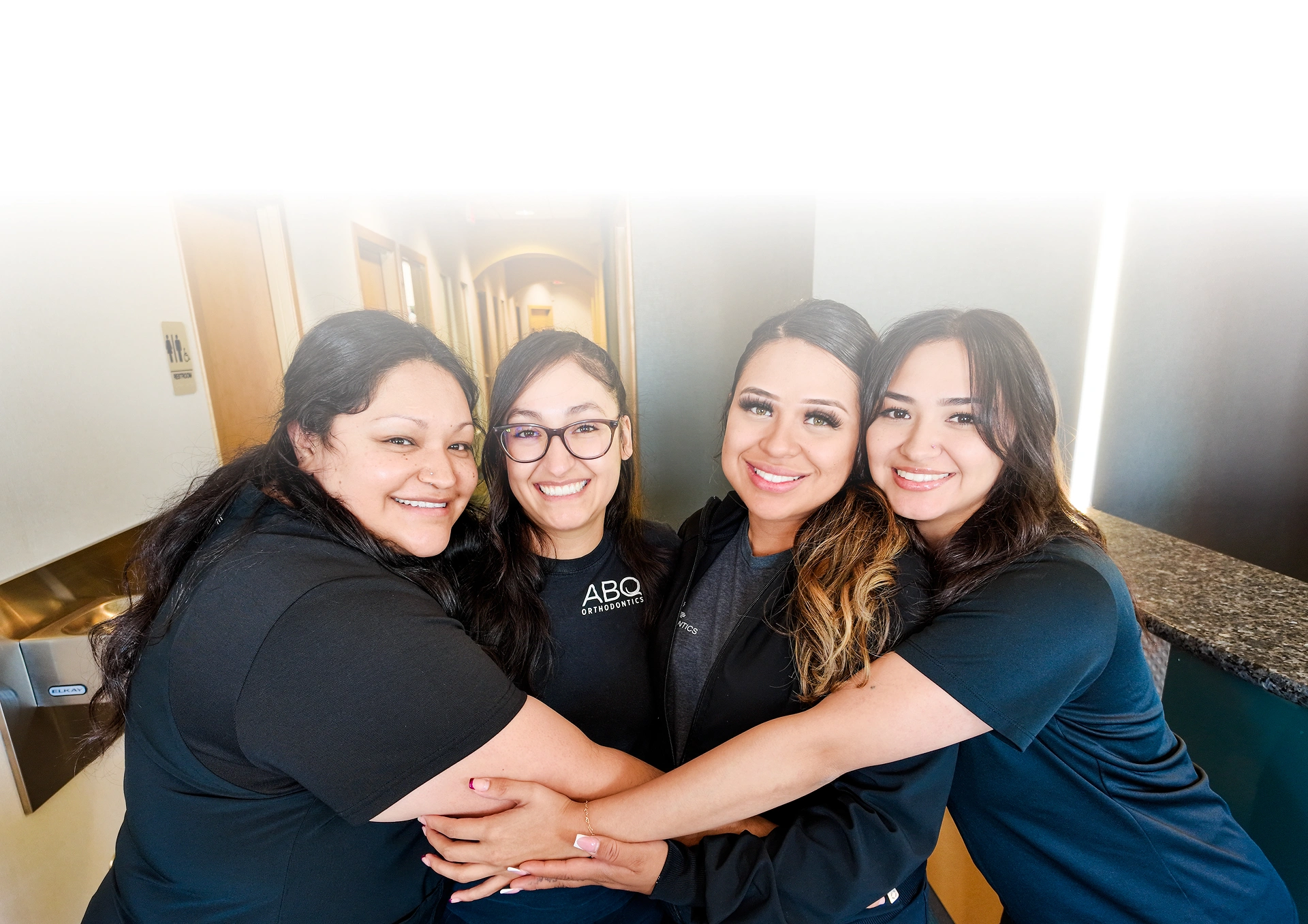 Four women team members at ABQ Orthodontics stacking hands together in office setting.