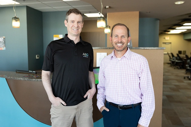 Two men standing together in modern orthodontic office with blue walls and reception desk.